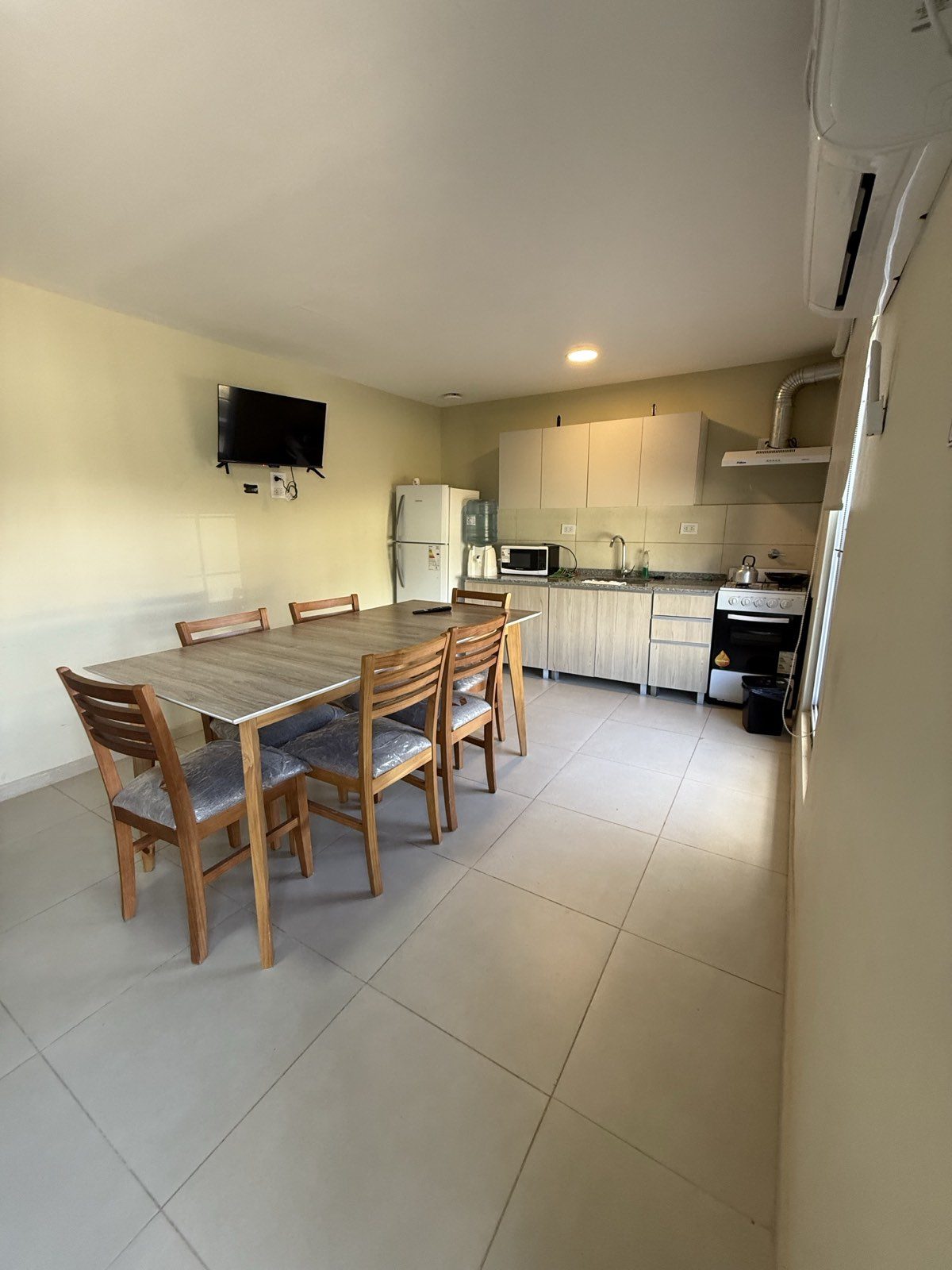 Cocina-comedor de la casa, con mesa para seis personas, televisor, heladera y cocina con horno