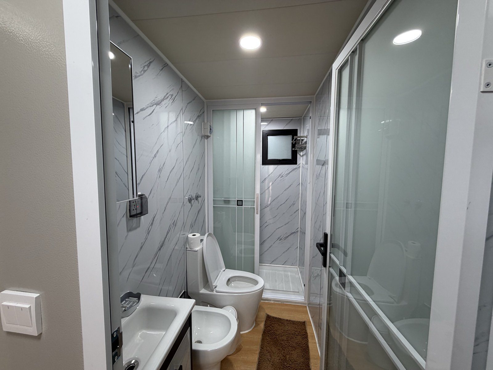 Ducha del baño del departamento, con revestimiento símil mármol y mampara de vidrio