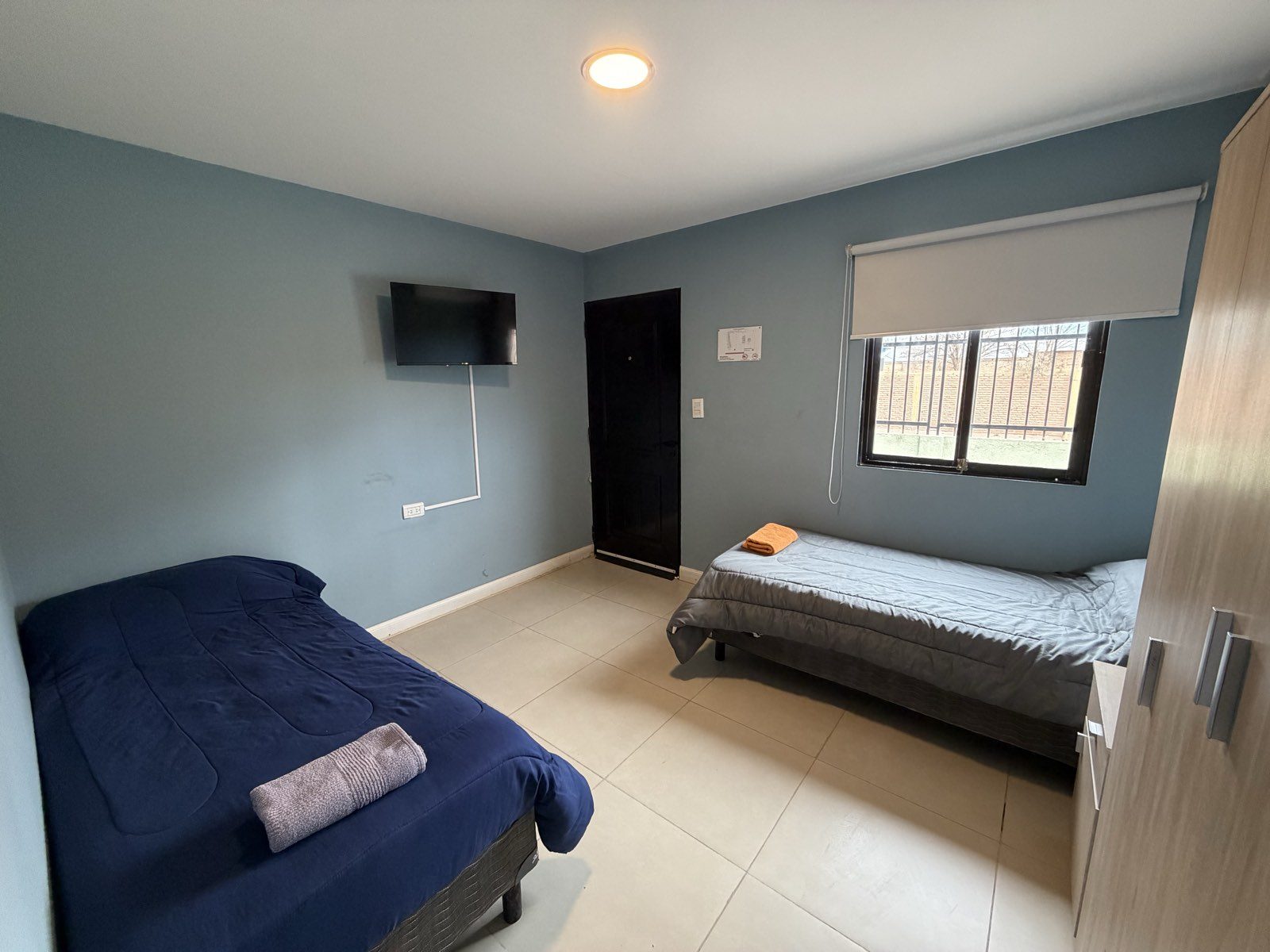 Habitación doble vista desde el otro extremo, con televisor y ventana al exterior