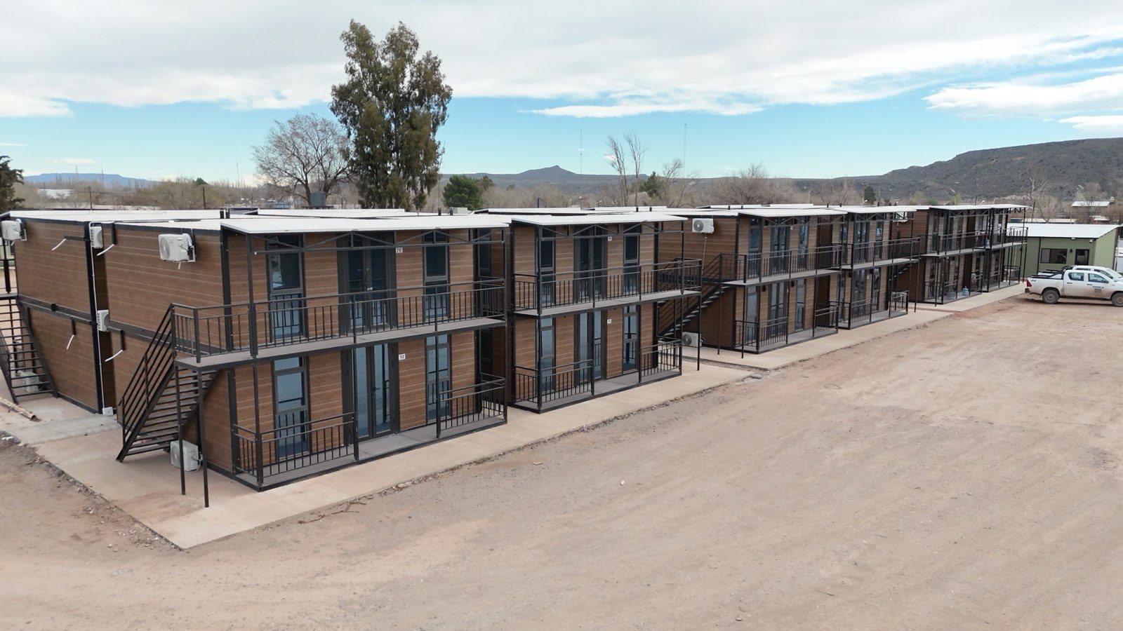 Conjunto de módulos de alojamiento alineados sobre la calle interna del complejo, con los cerros de fondo.